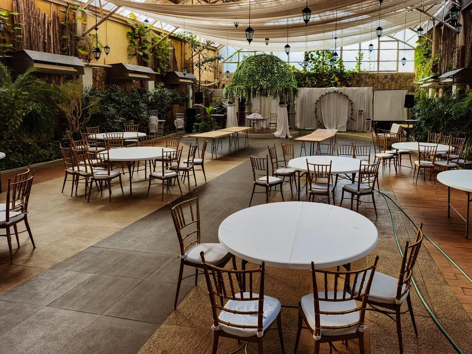 Conceptual empty event space with round tables, plants and warm overhead lights
